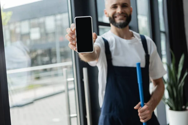 Unscharfe professionelle Reinigungskraft zeigt Smartphone mit leerem Bildschirm im Büro — Stockfoto