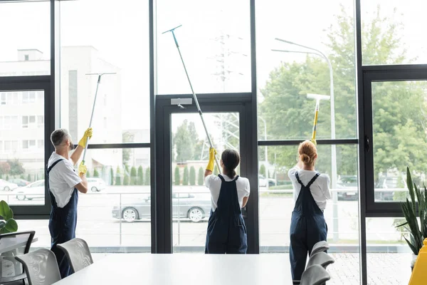 Back view of multicultural professional workers washing large panoramic windows in office — Stock Photo