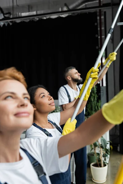 Junge Frau wäscht Fenster im Büro in der Nähe von Kollegen — Stockfoto