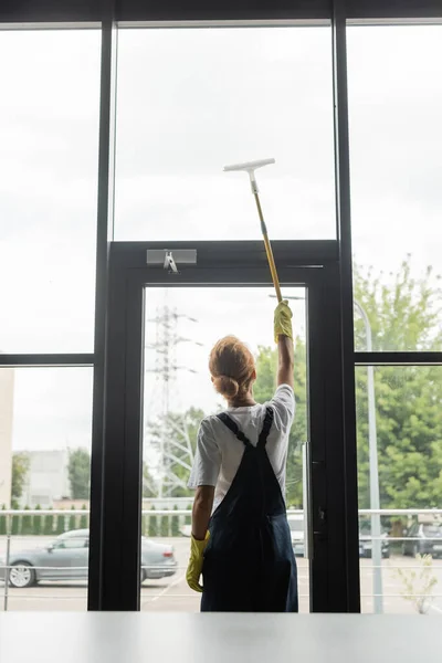 Vista trasera de la mujer en overoles lavando grandes ventanas en la oficina - foto de stock