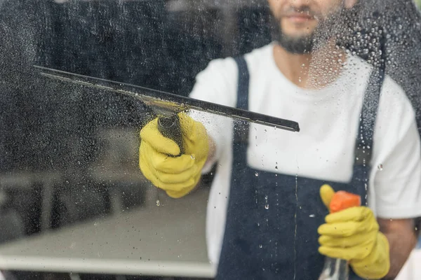 Cropped view of man with detergent and window wiper washing glass in office — Stock Photo