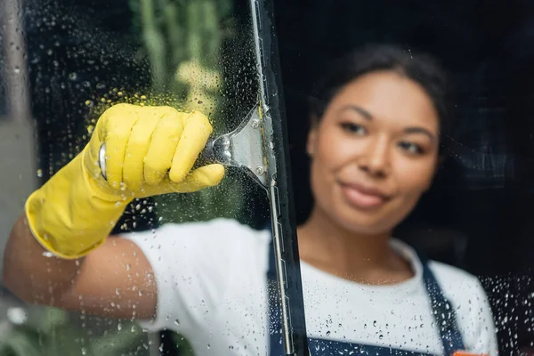 Verschwommene Frau in Gummihandschuhen, die Glas mit Scheibenwischer reinigt — Stockfoto