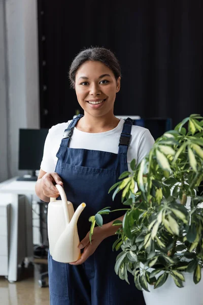 Щаслива бі-расова жінка з лійкою може дивитися на камеру біля зеленої рослини — стокове фото
