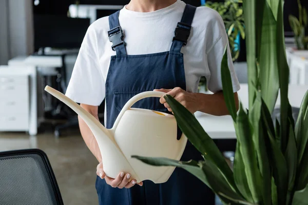 Vista cortada da mulher em pé uniforme com rega pode perto de planta verde — Fotografia de Stock