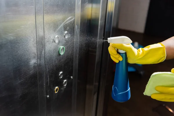 Vista ritagliata di detergente spray detergente sui pulsanti durante il lavaggio ascensore ufficio — Foto stock