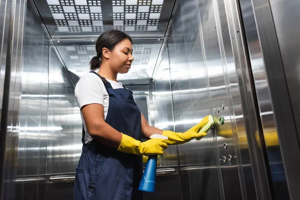 Jovem limpador bi-racial em roupas de trabalho lavando elevador de escritório com esponja — Fotografia de Stock