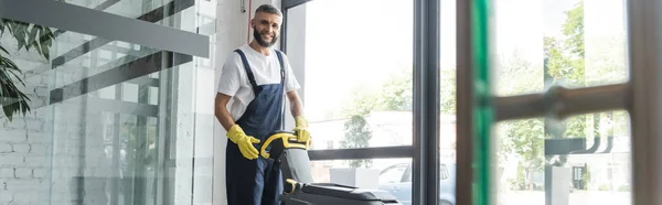 Limpiador profesional sonriendo a la cámara cerca de la máquina de fregar piso, pancarta - foto de stock