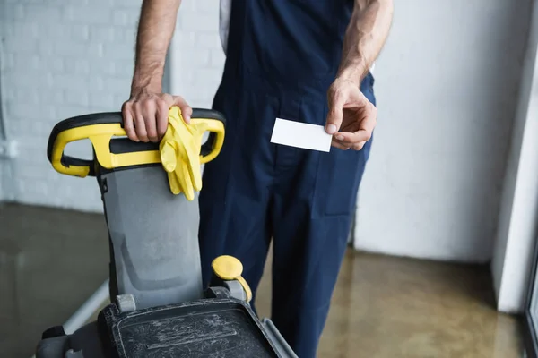 Visão parcial do homem em macacão segurando cartão de visita em branco perto da máquina de limpeza de piso — Fotografia de Stock