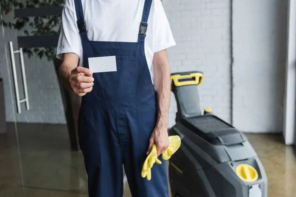 Teilbild eines Mannes in Overalls, der eine leere Visitenkarte in der Nähe eines professionellen Fußbodenwäschers hält — Stockfoto