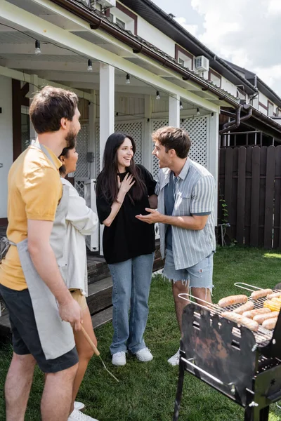Young man talking to friend near interracial people and grill in backyard — Stock Photo