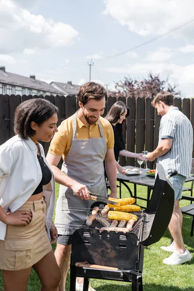 Alegre interracial amigos cocinar comida en la parrilla durante barbacoa en el patio trasero — Stock Photo