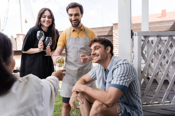 Positive man pouring wine near interracial friends in backyard — Stock Photo