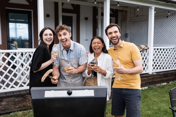 Positive interrassische Freunde mit Wein Blick auf Kamera in der Nähe Grill im Hinterhof — Stockfoto