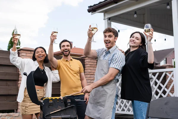 Amigos multiétnicos excitados segurando vinho e grelhando milho e carne ao ar livre — Fotografia de Stock