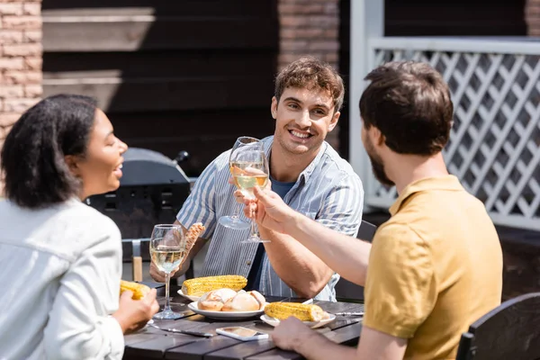 Uomini positivi clinking vino vicino al cibo e offuscata bi-razziale amico all'aperto — Foto stock