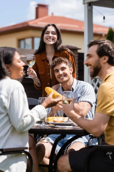 Sonrientes amigos interracial pasar tiempo durante la fiesta de barbacoa con vino al aire libre - foto de stock