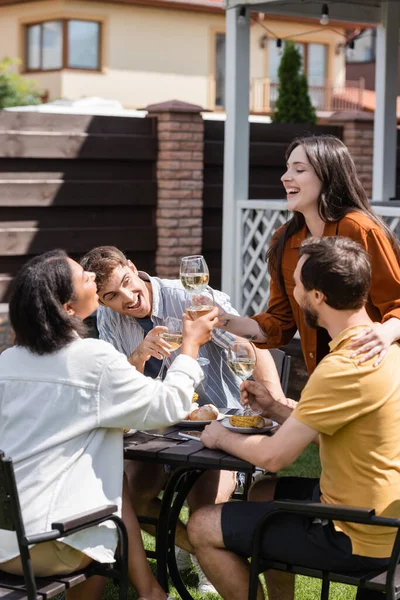 Amici multietnici positivi brindare con vino vicino al cibo durante il picnic in cortile — Foto stock