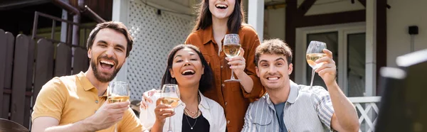 Alegres amigos multiétnicos sosteniendo copas de vino en el patio trasero, pancarta - foto de stock