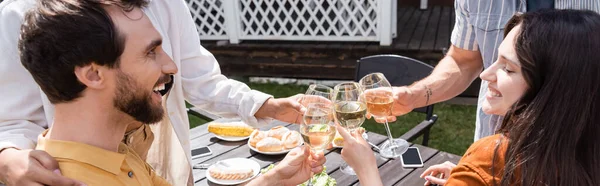 Amici allegri brindare con il vino vicino al cibo offuscato in cortile, striscione — Foto stock