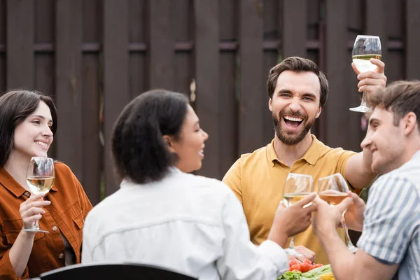 Excitado homem segurando vinho perto de amigos inter-raciais durante bbq festa ao ar livre — Fotografia de Stock