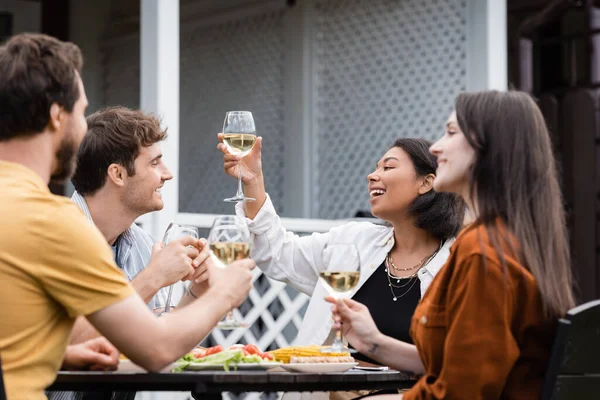 Happy bi-racial woman toasting with glass near friends during bbq party in backyard — Stock Photo