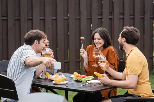 Cheerful multiethnic friends taking selfie while laughing during bbq party in backyard — Stock Photo