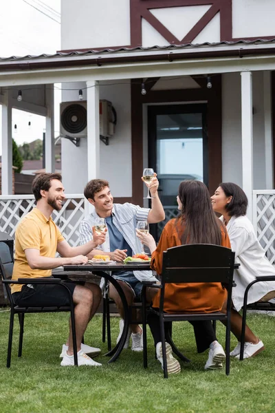 Homem feliz levantando copo de vinho perto de amigos inter-raciais durante a festa bbq no quintal — Fotografia de Stock