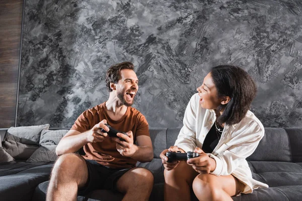 QUIIV, UCRÂNIA - JULHO 26, 2022: amigos inter-raciais felizes segurando joysticks e olhando um para o outro — Fotografia de Stock