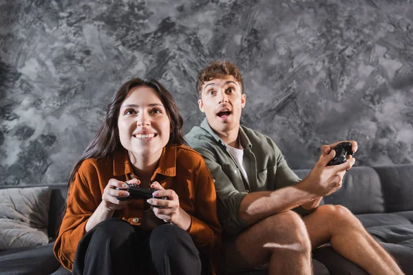 KYIV, UCRAINA - 26 LUGLIO 2022: amici allegri che tengono i joystick e giocano ai videogiochi seduti sul divano grigio — Foto stock
