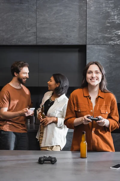 KIEW, UKRAINE - 26. JULI 2022: Fröhliche Frau spielt Videospiel, während sie den Steuerknüppel in der Nähe multiethnischer Freunde hält — Stockfoto