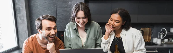 Happy woman holding laptop near multiethnic friends in kitchen, banner — Stock Photo