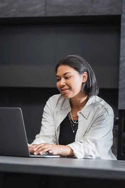 Happy bi-racial woman using laptop while working remotely in kitchen — Stock Photo