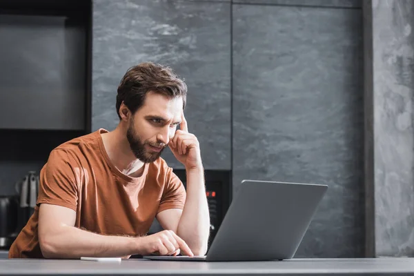 Barbudo freelancer utilizando portátil portátil mientras está sentado en la cocina — Stock Photo