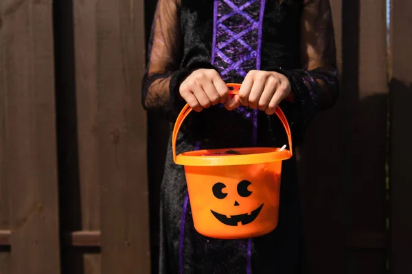 Cropped view of girl in witch costume holding halloween bucket outdoors — Stock Photo