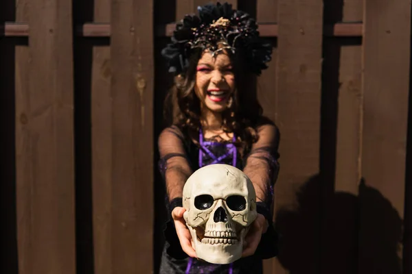Happy girl in witch halloween costume holding spooky skull on blurred background — Stock Photo