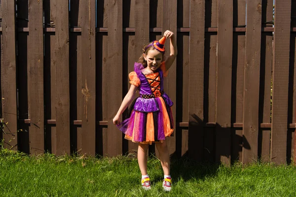 Mädchen im Clown-Halloween-Kostüm berührt Partymütze und zeigt wütende Fratze — Stockfoto