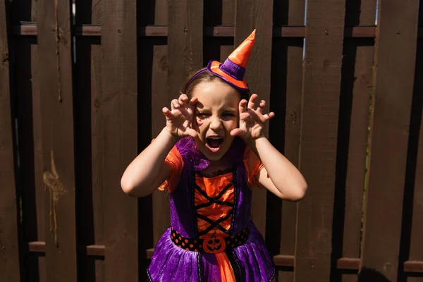 Chica en traje de Halloween mirando a la cámara con mueca enojada y mostrando gesto aterrador - foto de stock