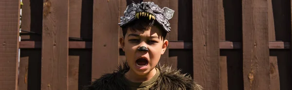 Asian boy with scary grimace growling and looking at camera outdoors, banner — Stock Photo