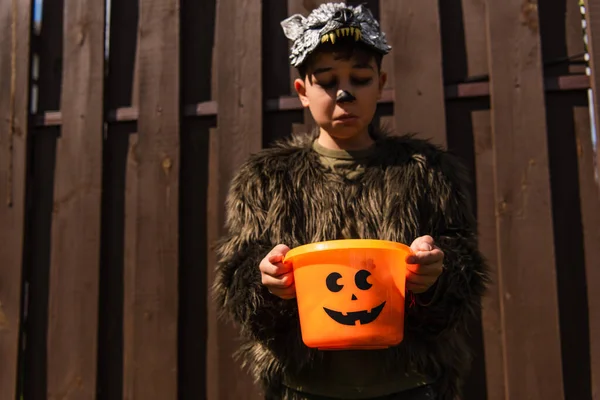 Offended asian boy in werewolf costume looking into empty halloween bucket — Stock Photo