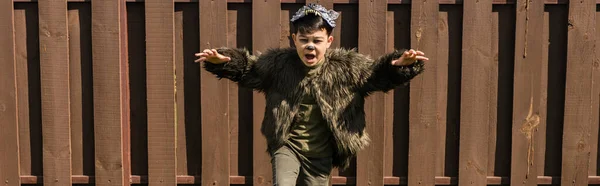 Asiático chico en hombre lobo halloween traje corriendo y gruñendo en backyard, banner - foto de stock