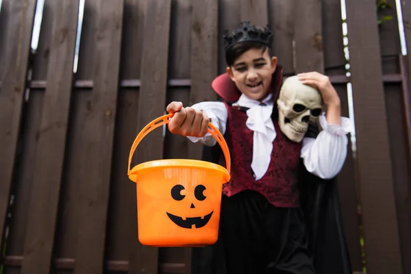 Foco seletivo de truque ou tratar balde na mão de menino asiático desfocado no traje halloween — Fotografia de Stock