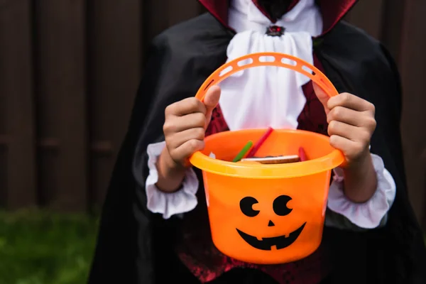 Recortado vista de niño en halloween traje celebración truco o tratar cubo con dulces - foto de stock