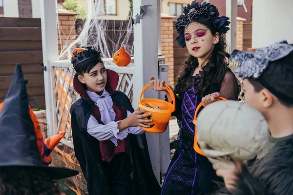 Ragazza che tiene secchi vicino agli amici multietnici in costumi di Halloween in cortile — Foto stock