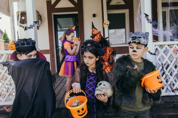 Багатоетнічні діти в костюмах Хеллоуїна тримають відра біля азіатського друга на задньому дворі — стокове фото