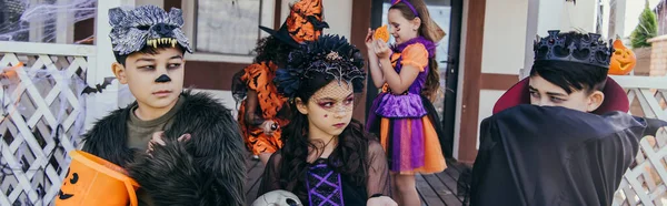 Asiatique garçon en costume regarder amis avec seau pendant Halloween célébration à l'extérieur, bannière — Photo de stock