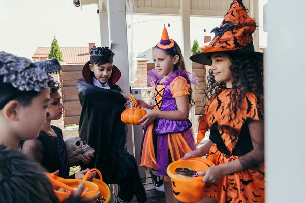 Sonriendo niños multiétnicos sosteniendo cubos y calabaza durante la celebración de Halloween al aire libre - foto de stock