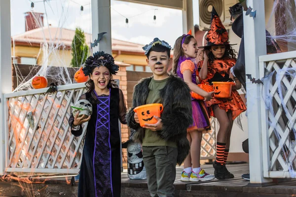 Позитивні багатоетнічні діти тримають череп і відро під час святкування Хеллоуїна з друзями на відкритому повітрі — стокове фото