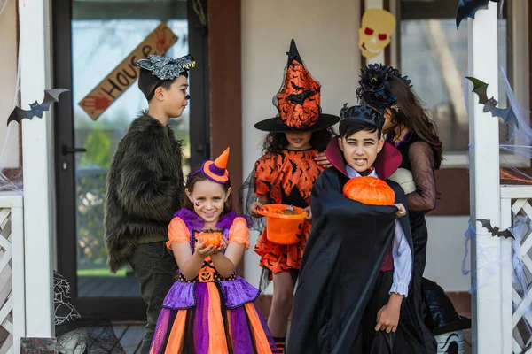 Multiethnic kids in halloween costumes holding pumpkins near friends in backyard — Stock Photo