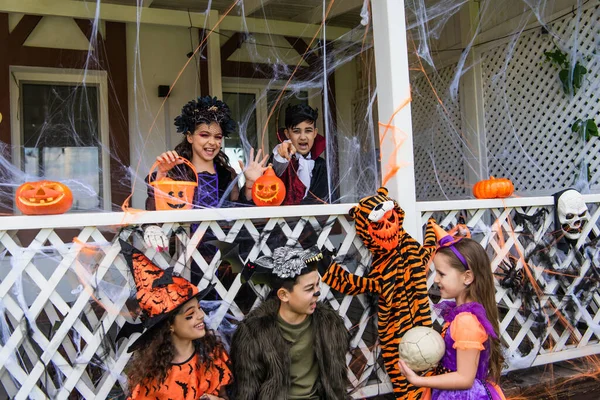Interracial niños en halloween trajes hablando cerca de la decoración en casa - foto de stock