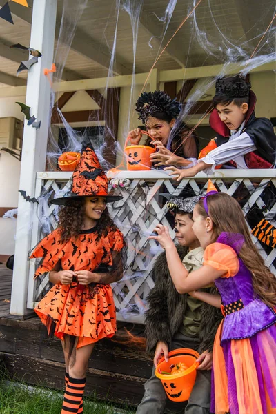 Multiethnische Kinder in Halloween-Kostümen grimmig neben Freund mit Hexenhut im Freien — Stockfoto